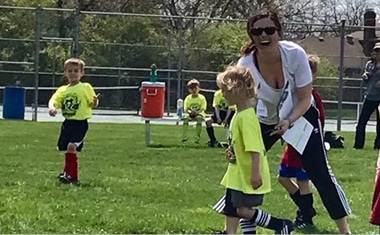 Jennie Carr (smiling white brunette woman in white T-shirt and black capris) with her arm around a child in a yellow JCC soccer T-shirt