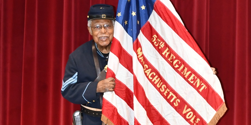 Andrew Bowman, an elderly black man, wearing a Civil War uniform and carrying the flag bearing the name of the regiment his grandfather, Andrew Jackson Smith, belonged to