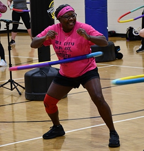 A Black woman in a bright pink headband and T-shirt hula hooping in Total Body BoxJUMP group ex class