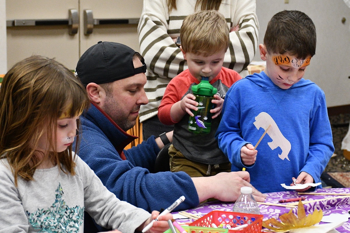 A man and three children coloring at a family engagement event